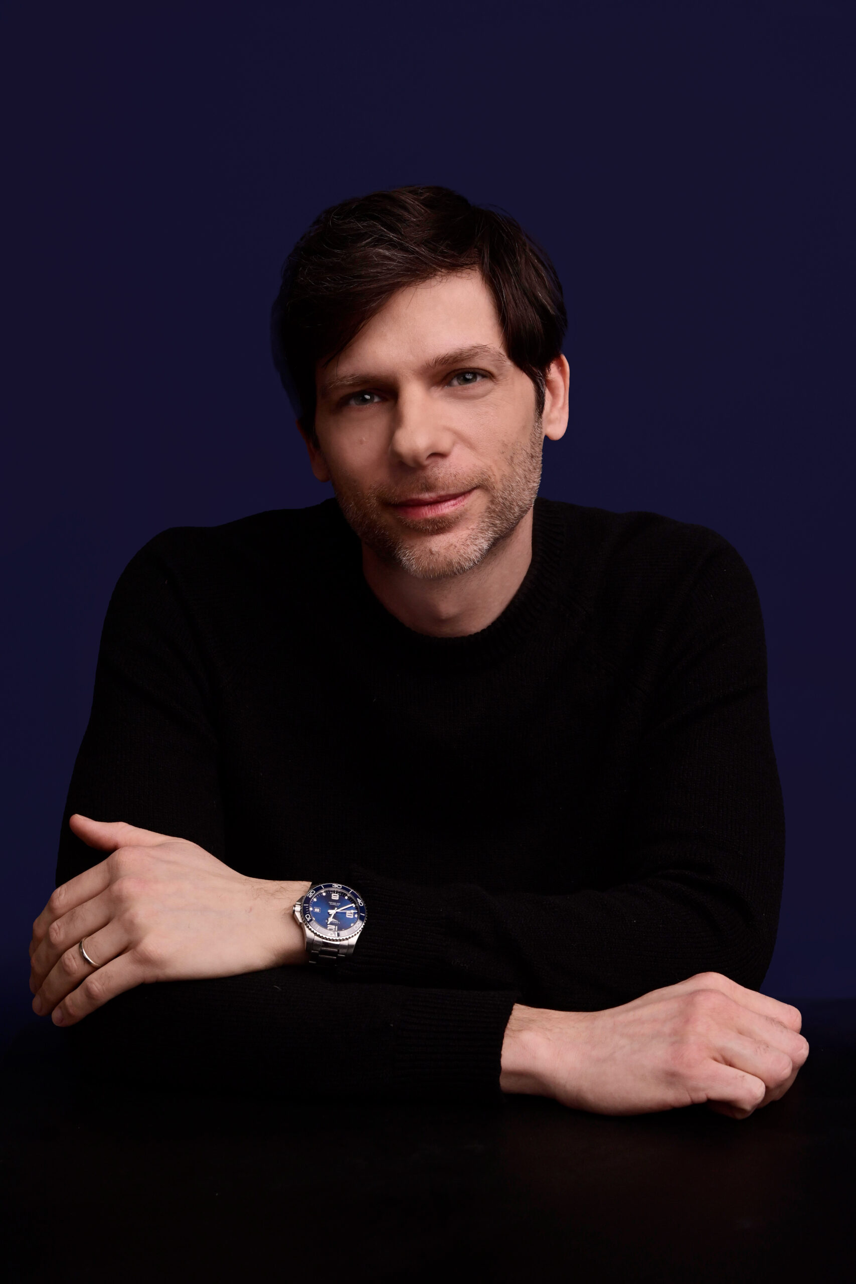 Morr Meroz in a black sweater, arms folded on a table, looking at the camera.